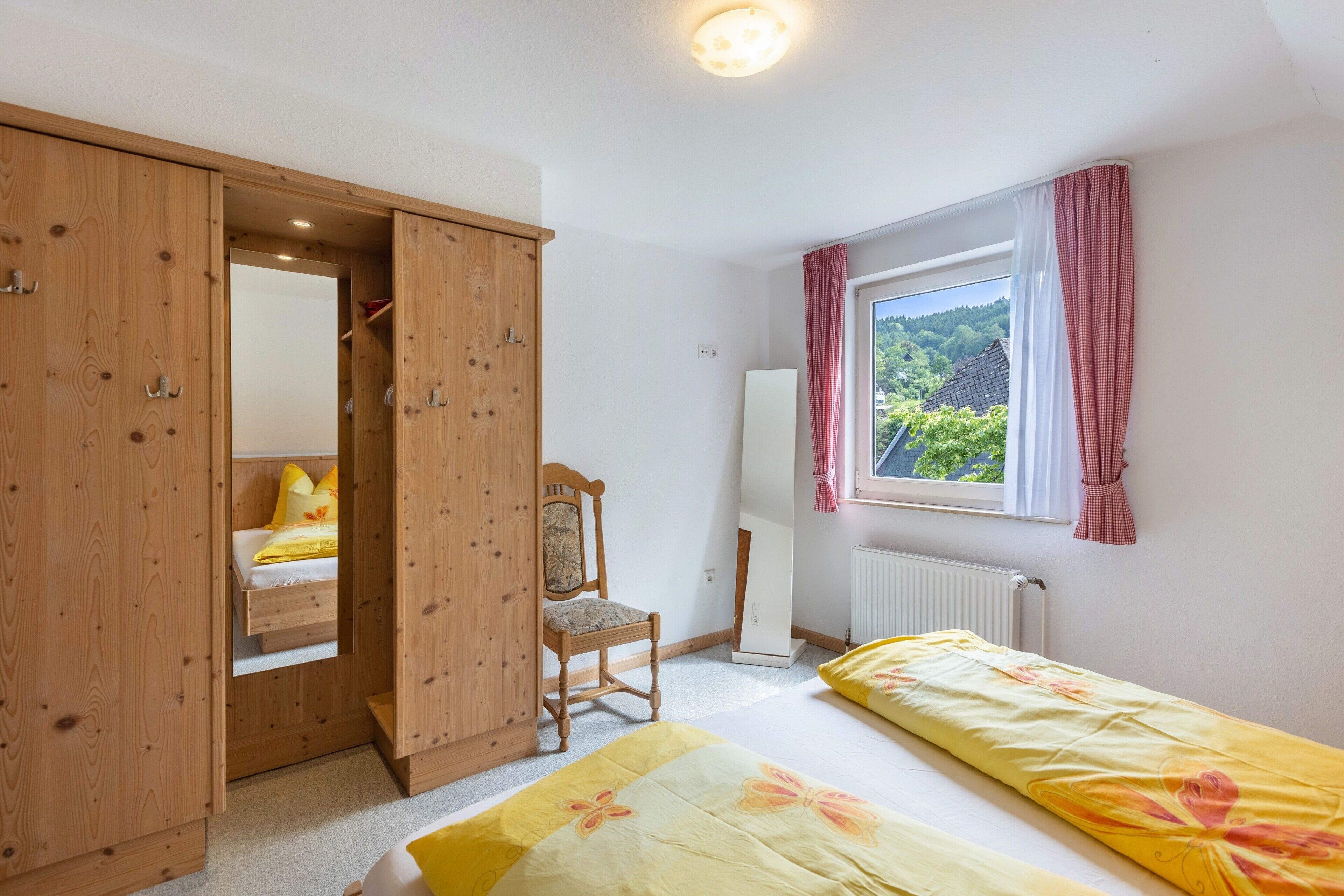 A bedroom with a wooden wardrobe, a single bed, a chair, a window with a view, and a radiator.