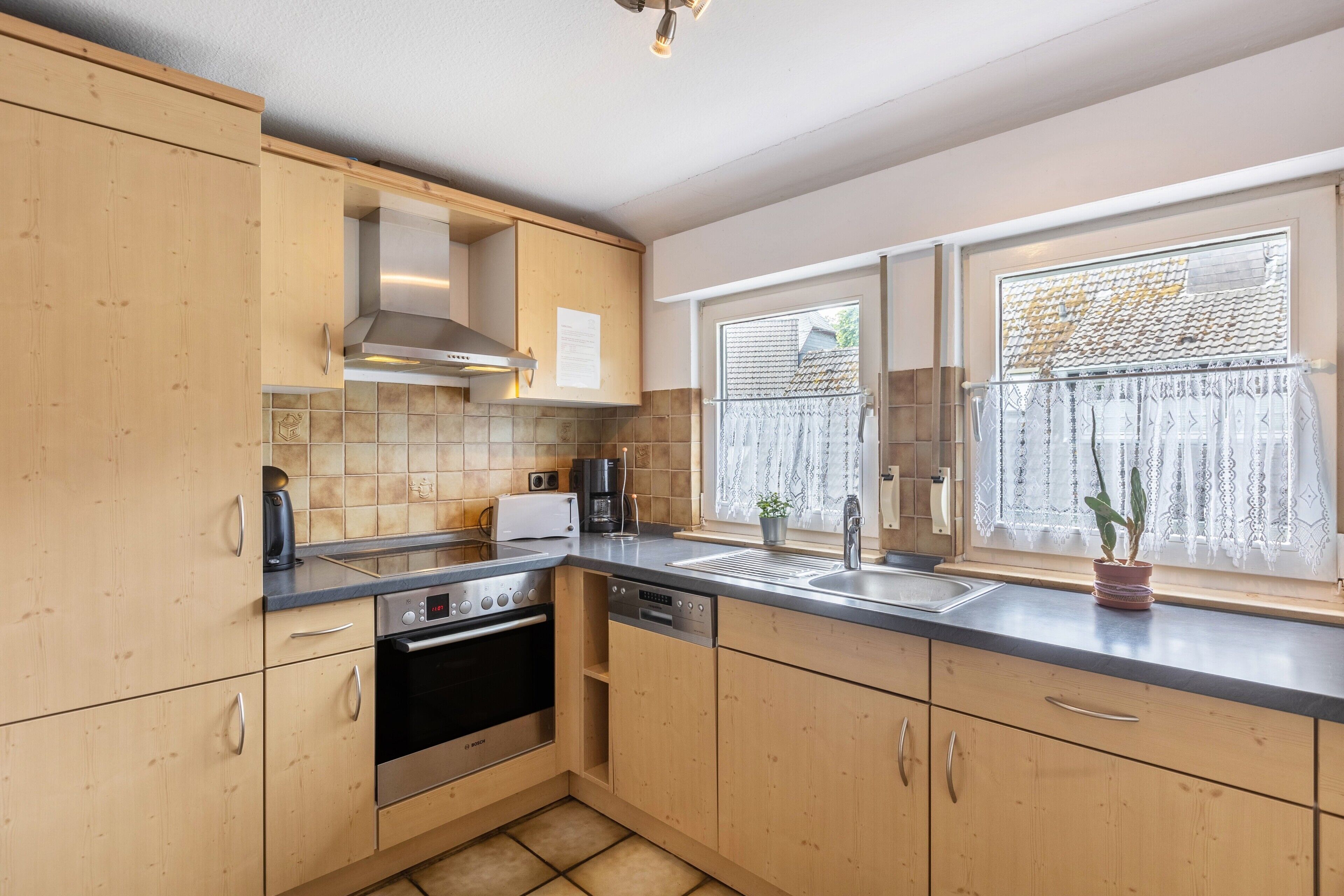A modern kitchen with wooden cabinets, a stainless steel range, a dishwasher, and a window with a view.