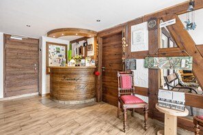 A reception area with a wooden reception desk, a red cushioned chair, and a wooden wall with various signs and decorations.
