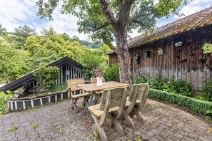 A rustic wooden table and chairs set on a cobblestone patio with a wooden fence and a tree in the background.