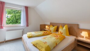 A bedroom with a wooden headboard, a window with red curtains, a radiator, and a bed with yellow floral bedding.