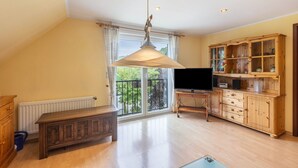 Ett rymligt vardagsrum med ett stort fönster, ett träskåp, en tv och en hängande lampa.