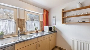 A kitchen with a sink, a microwave, a potted plant, and a window with curtains.