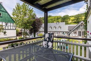 A balcony with a metal table and a chair, overlooking a village with traditional houses and a green hill in the background. - Apartment 'Sonnenschein' with Private Terrace, Balcony and Wi-Fi (Lennestadt)