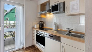 Una cuina moderna amb forn, microones i cafetera integrats, un taulell de fusta i vista d'un edifici verd a l'exterior.