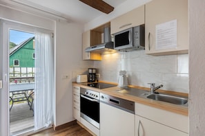 A modern kitchen with a built-in oven, microwave, and coffee maker, a wooden countertop, and a view of a green building outside.