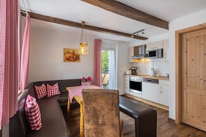 A cozy living room with a sofa, table, and chairs, a kitchen with modern appliances, and a wooden ceiling.