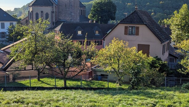 Uma igreja histórica com uma torre imponente, rodeada por edifícios residenciais e um campo gramado.