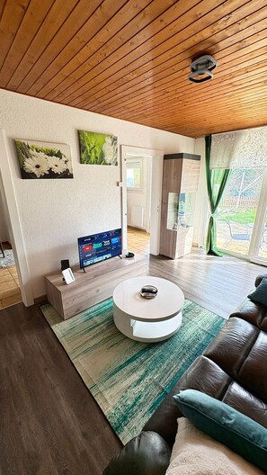 A modern living room with a wooden ceiling, a round coffee table, a leather sofa, and a TV displaying a sports channel. - Le Refuge du Cerisier - Tranquillity and an Alpine View in La Chaux-de-Fonds (La Chaux-de-Fonds)