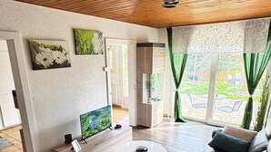Een moderne woonkamer met een houten plafond, een bruine leren bank, een ronde salontafel en een televisie.