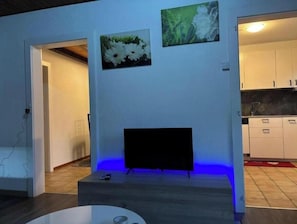 Ein Wohnzimmer mit einem Flachbildfernseher auf einem Schrank, einem Couchtisch und zwei an der Wand hängenden Bildern.