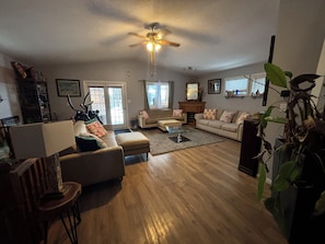A spacious living room with hardwood flooring, a ceiling fan, a fireplace, and a large window.
