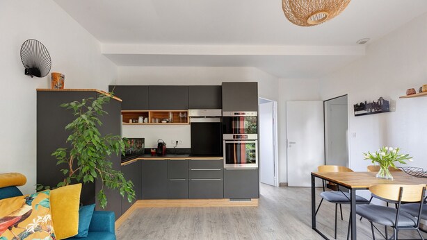 Eine moderne Küche mit dunklen Schränken, einem Einbauofen und einem Essbereich mit Holztisch und Stühlen.