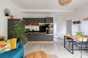 Een moderne keuken met donkere kastjes, een ingebouwde oven en een eethoek met een houten tafel en stoelen.