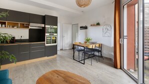 Eine moderne Küche mit dunklen Schränken, ein Essbereich mit Holztisch und -stühlen sowie eine große Schiebeglastür, die zu einem Außenbereich führt.
