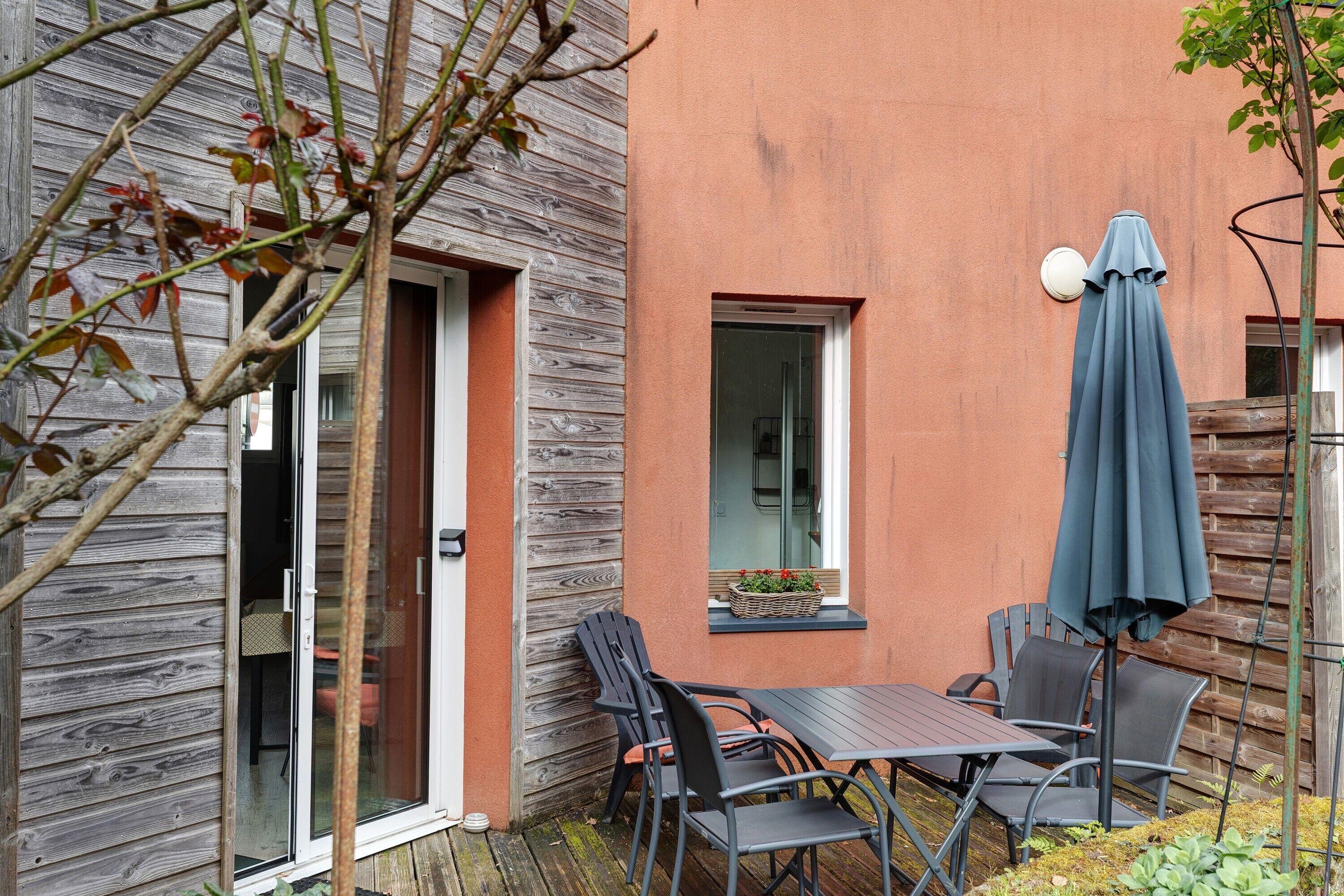 An outdoor patio with a table and chairs, a sliding glass door, and a window with a view.