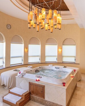 Une salle de spa dotée d’un grand jacuzzi, d’un escalier en bois et de fenêtres en arc de cercle.