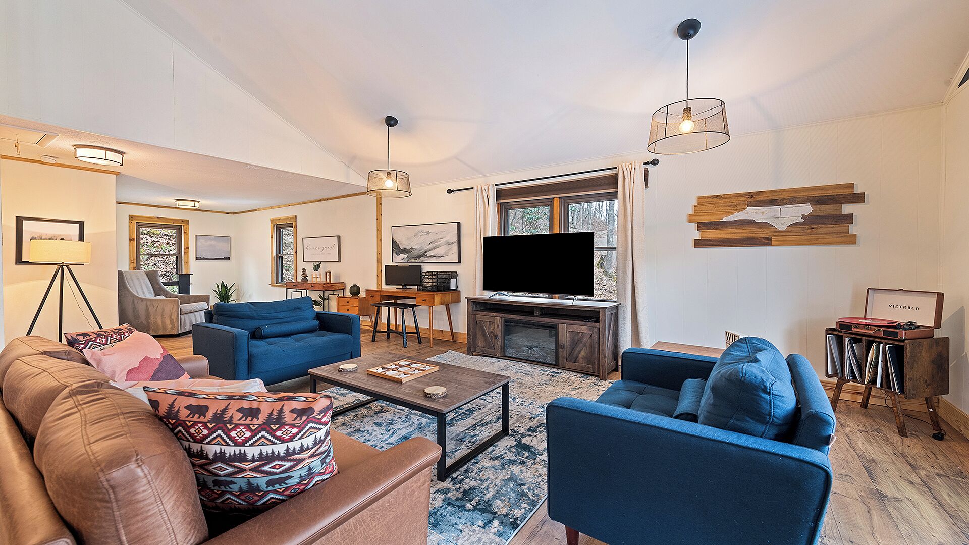 Una sala de estar moderna con un televisor grande, sofás azules, una mesa de centro y un mueble de madera para entretenimiento.