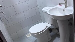 Ein kleines, kompaktes Badezimmer mit weißen Fliesen, einer weißen Toilette und einem weißen Waschbecken.