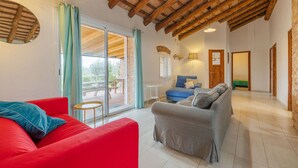 Uma sala de estar ampla com um sofá vermelho, um sofá cinza e um sofá azul. Teto de madeira e uma porta de vidro deslizante que dá para um pátio externo.