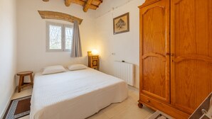 Quarto com cama, guarda-roupa de madeira, janela com cortinas e radiador.