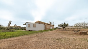 Uma propriedade rural com um edifício branco, entrada de cascalho e vegetação escassa.