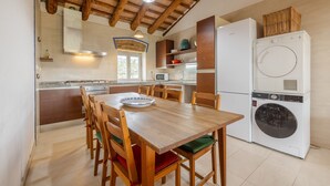 Uma cozinha com armários de madeira, uma mesa de jantar com cadeiras, uma máquina de lavar e um ventilador de teto.