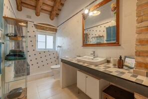 A bathroom with a glass shower enclosure, a white toilet, a sink with a mirror above it, and a tiled floor.