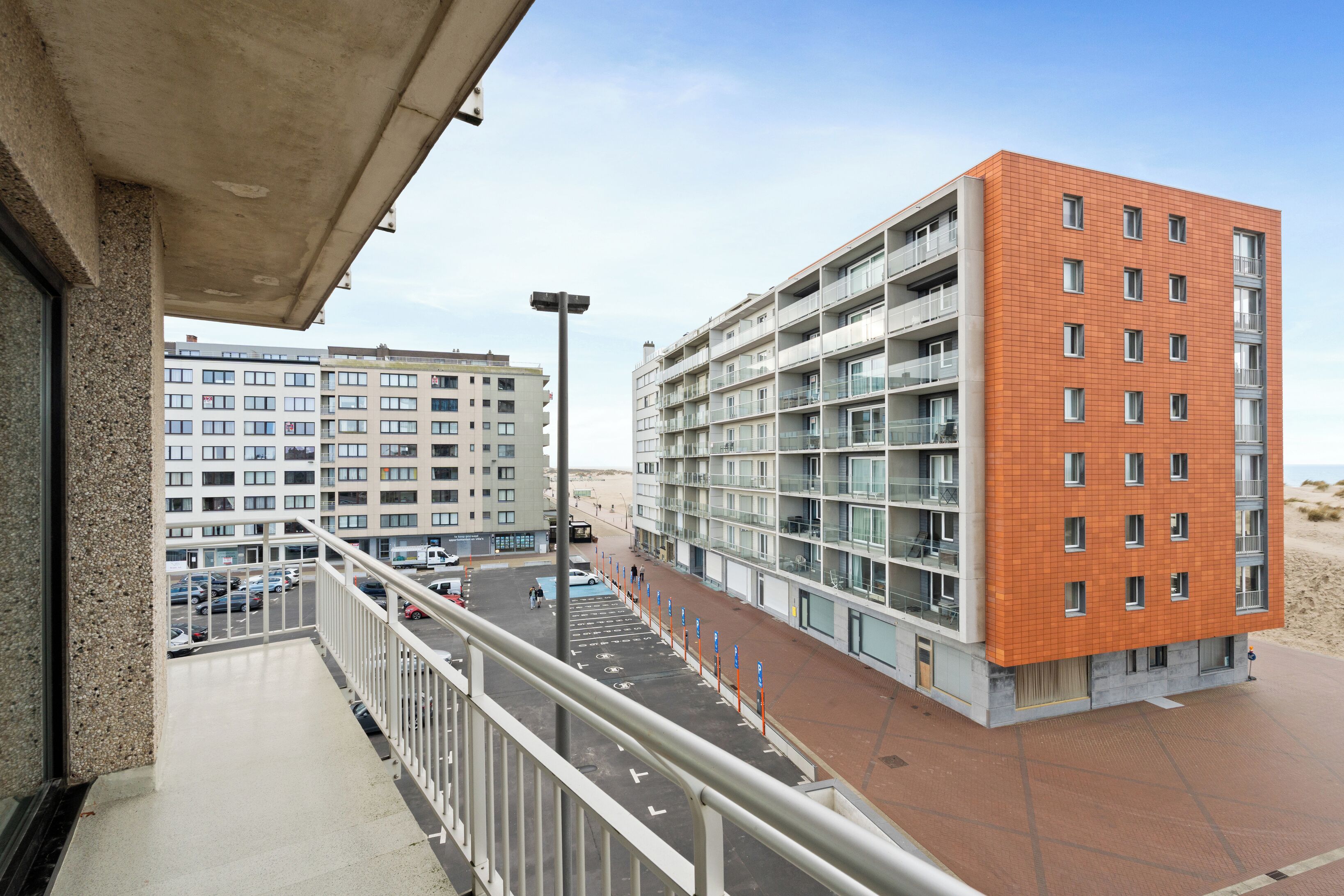 A modern building with multiple floors, balconies, and a parking area.
