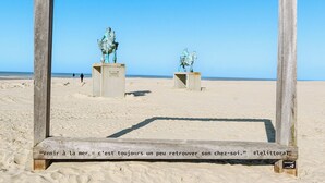 Een houten frame met twee bronzen beelden van een ruiter op een zandstrand.