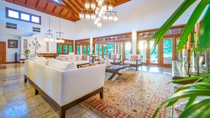 A spacious living room with a high ceiling, large windows, and a chandelier.