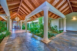 Une allée couverte avec un sol en pierre, des colonnes blanches et un plafond en bois.