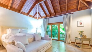 A bedroom with a bed, a sofa, a small table, and a view of greenery through a glass door.