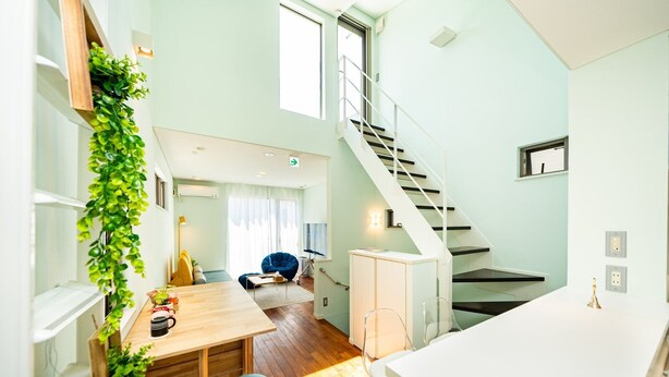 Une cuisine moderne avec une table en bois, deux chaises bleues, un plan de travail blanc et un escalier menant à un autre niveau.
