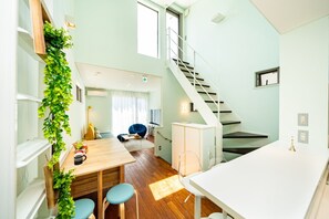 A modern kitchen with a wooden table, two blue chairs, a white countertop, and a staircase leading to another level.