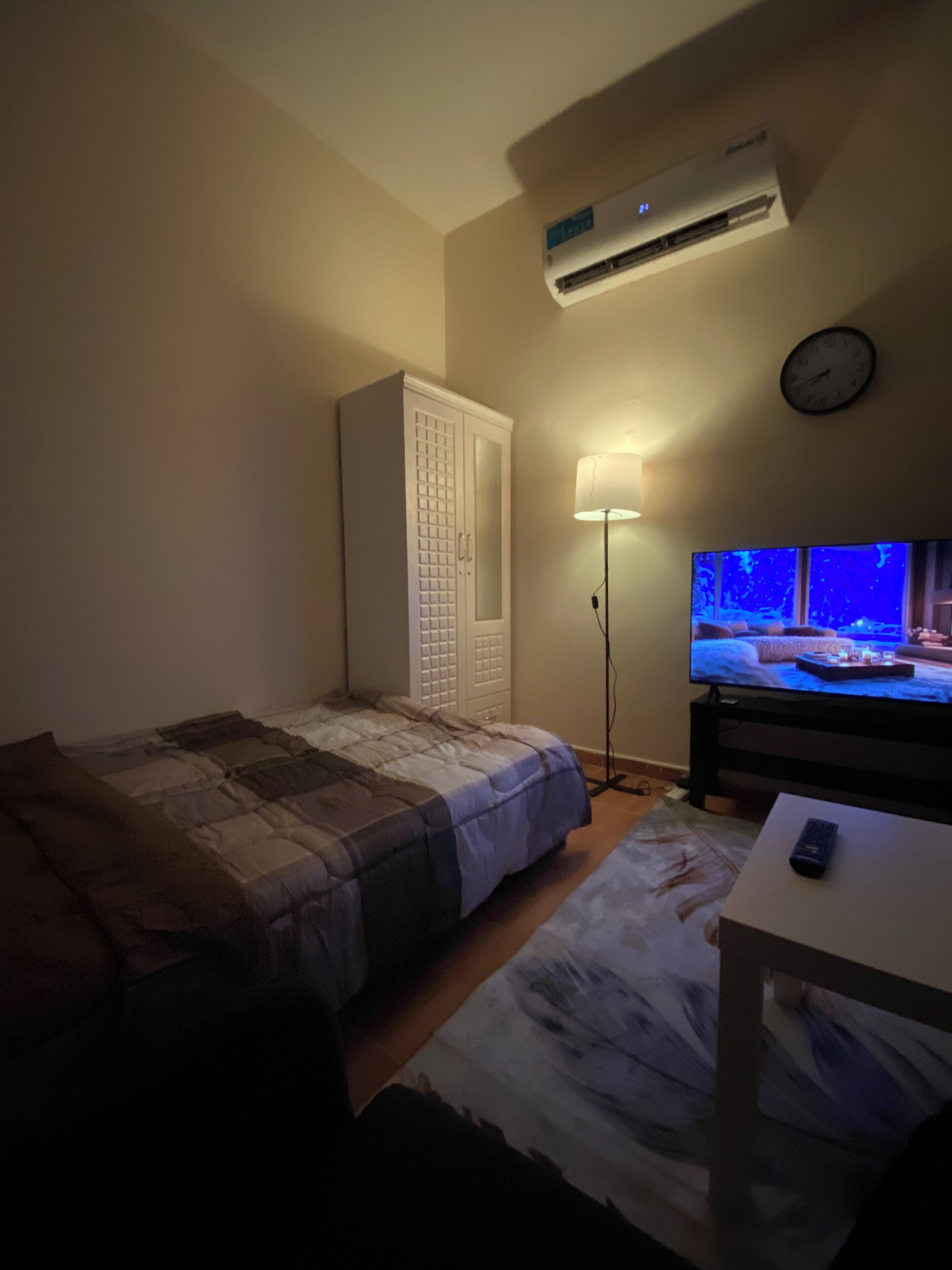 A bedroom with a bed, a wardrobe, a TV, and an air conditioner.