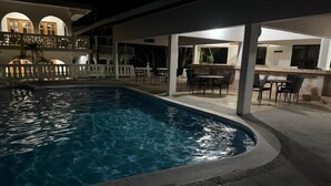 Ein Schwimmbad mit überdachter Terrasse, einer Bar und Außenbereich mit Sitzgelegenheiten.
