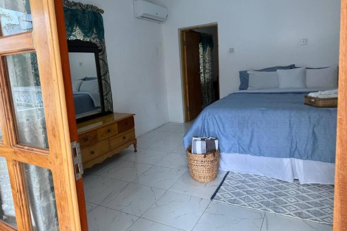 Un dormitorio con cama, cómoda, espejo, ventana con cortinas y aire acondicionado instalado en la pared.