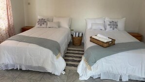 Ein Zimmer mit zwei Betten, jeweils mit weißer Bettwäsche und dekorativen Kissen. Auf dem Boden zwischen den Betten steht ein Korbwäscheschrank.