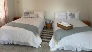 Ein Zimmer mit zwei Betten, jeweils mit weißer Bettwäsche und dekorativen Kissen, einem Korbwannenkorb auf dem Boden und einem Streifen Teppich.