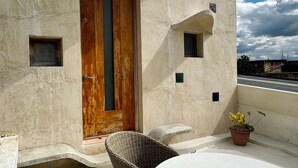 Eine Dachterrasse mit rundem Tisch, Korbstühlen und einer Holztür, sowie einem kleinen Topfpflanzen.