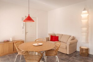 Ein Essbereich mit einem runden Holztisch, Korbstühlen, einem beigen Sofa und einer roten Pendelleuchte.
