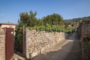 A narrow stone pathway flanked by a stone wall and a wooden gate, leading to a residential area with houses and greenery. - Il Faro – Design and Relaxation on Lake Garda (Torri del Benaco)