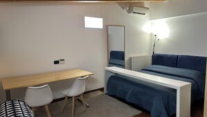 Un dormitorio con cama, escritorio, dos sillas, espejo y radiador.