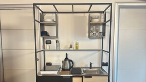 Cocina compacta con encimera negra, hervidor y estantes superiores para almacenamiento.