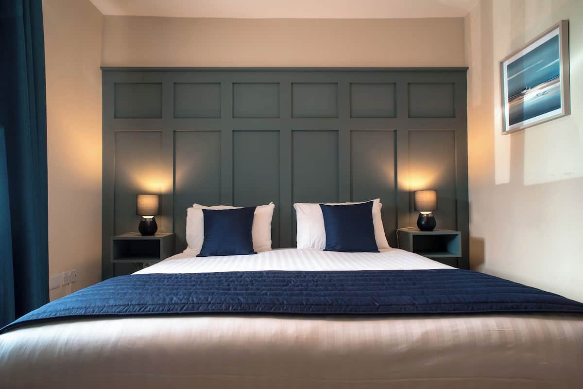 A hotel room with a large bed, two bedside lamps, a headboard, and a framed picture on the wall.