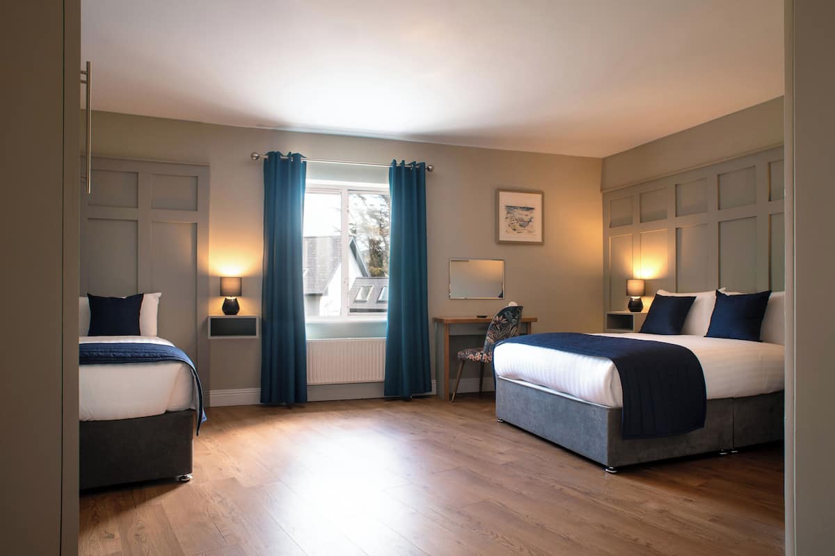A hotel room with two beds, a desk, a chair, and a window with curtains.