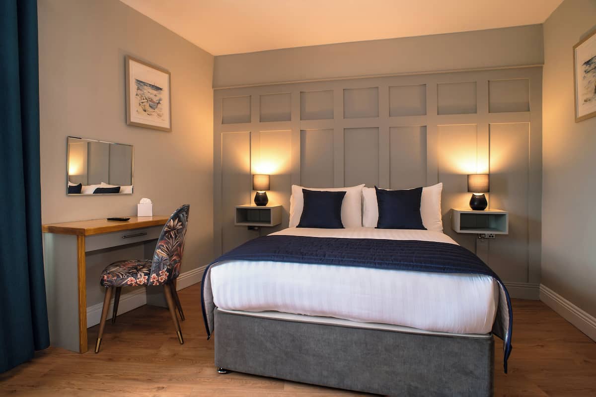 A hotel room with a bed, desk, chair, bedside lamps, and a framed picture on the wall.