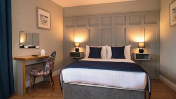 A hotel room with a bed, desk, chair, bedside lamps, and a framed picture on the wall.
