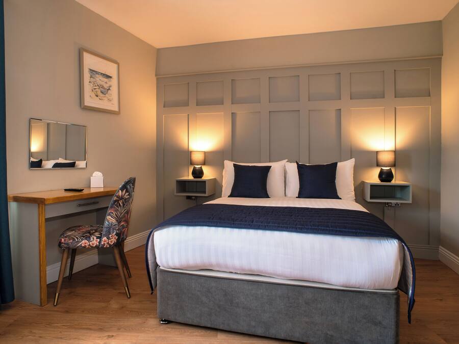 A hotel room with a bed, desk, chair, bedside lamps, and a framed picture on the wall.
